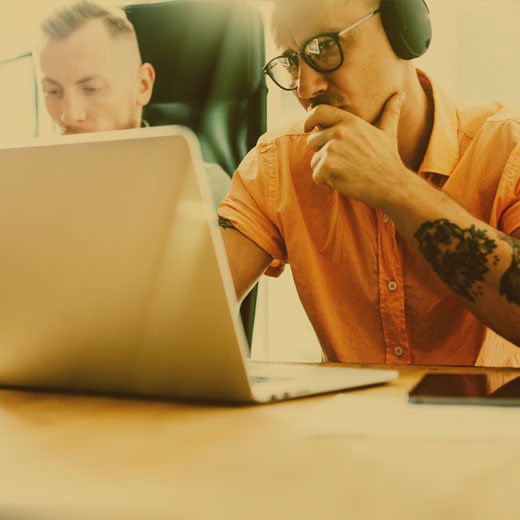 Two men one with tattoos focused on laptop seo and ppc